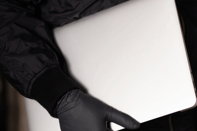 A person carrying a silver laptop with a gloved hand.
