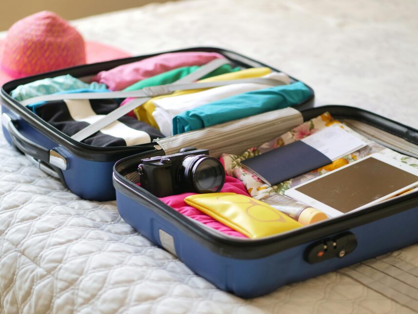 A suitcase open on a bed, neatly packed with bright clothes, a camera and passport.