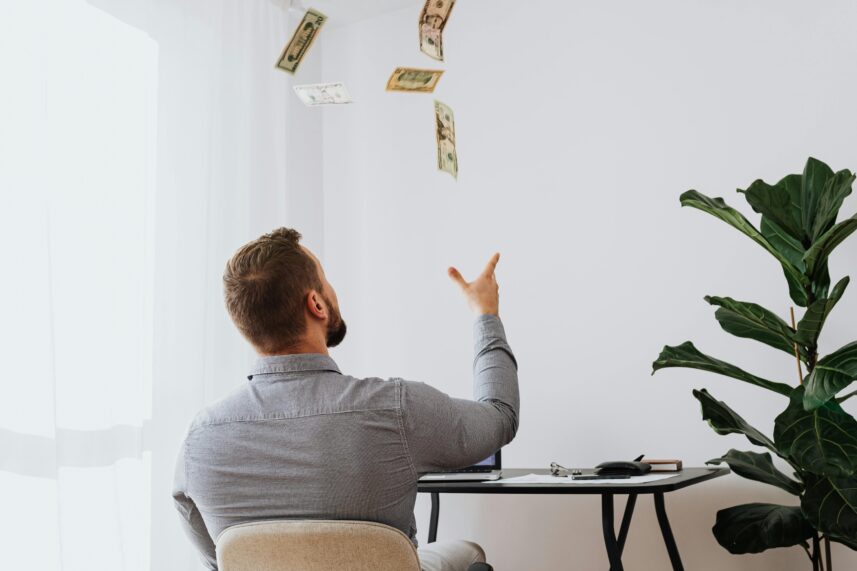 A man sat at a desk throwing money into the air