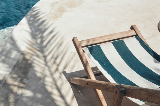 A striped deckchair in the sun next to a swimming pool.